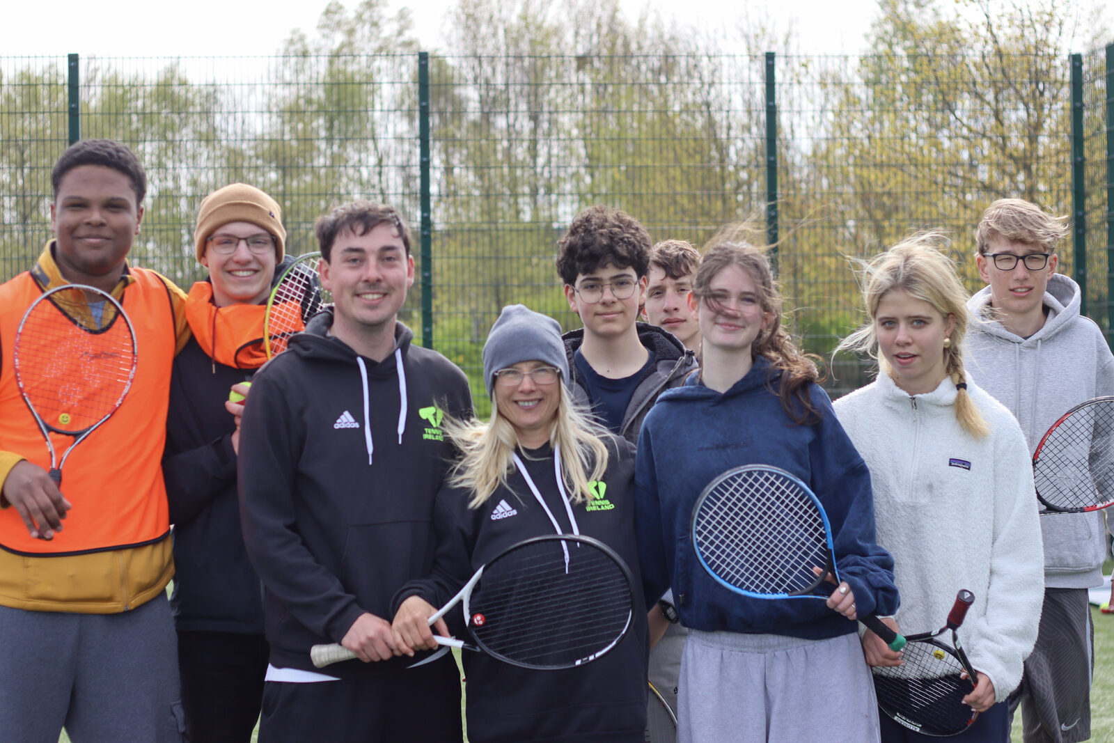 A smiling group of young people and S'port for Grief volunteers together with tennis rackets at an event